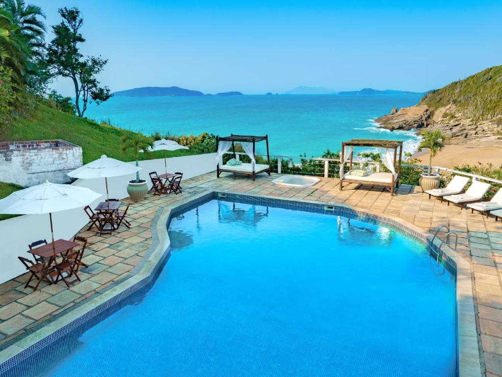 a swimming pool with chairs and umbrellas next to the beach at Apa Pau Brasil in Búzios