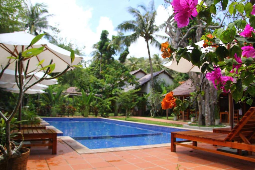 a swimming pool with two benches and pink flowers at La Mer Resort, Phú Quốc in Phú Quốc