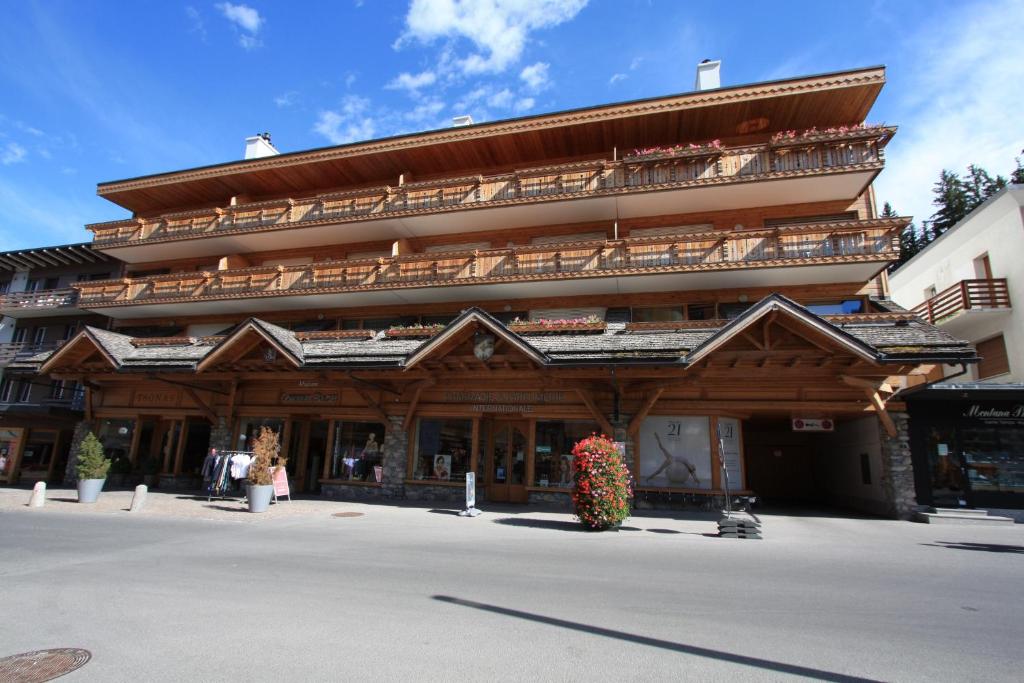 Un grand bâtiment en bois avec balcon se trouve dans une rue. dans l'établissement Apartment International, à Crans-Montana