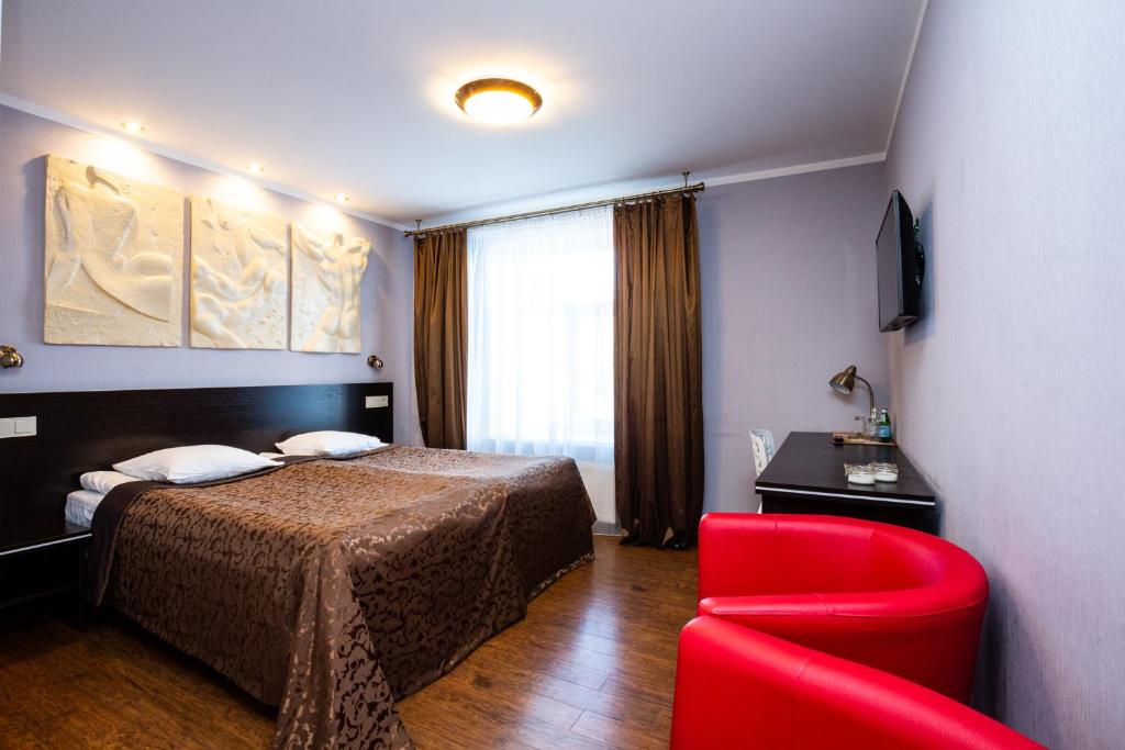 um quarto de hotel com uma cama e uma cadeira vermelha em Primo Hotel em Riga