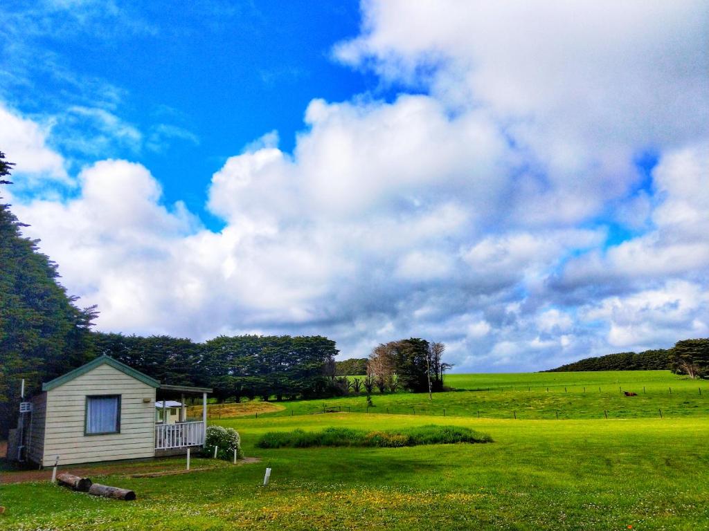 a small house on a green field with a cloudy sky at Twelve Apostles Motel & Country Retreat in Princetown