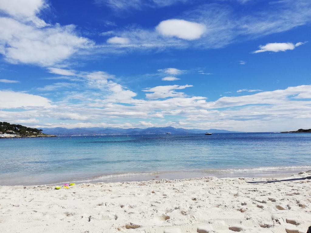 a beach with the ocean and a blue sky and clouds at Hotel Miramar- Cap d'Antibes - La Garoupe plage in Antibes