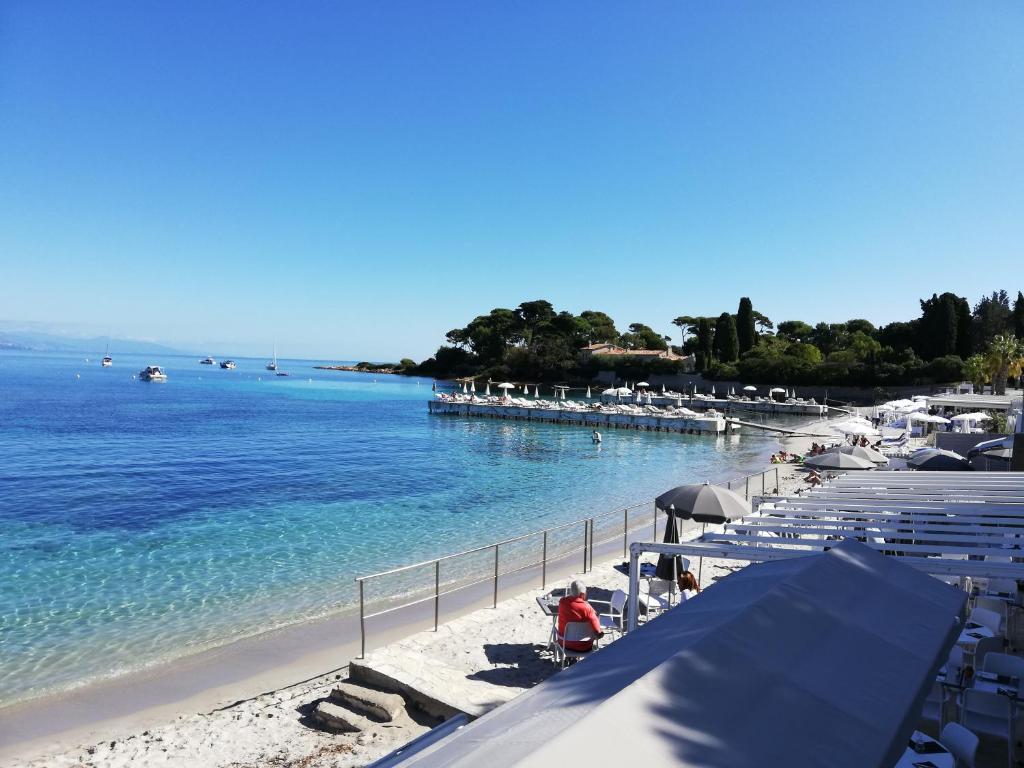 a beach with white umbrellas and boats in the water at Hotel Miramar- Cap d'Antibes - La Garoupe plage in Antibes