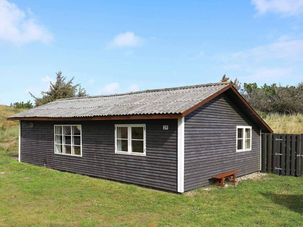 una pequeña casa negra en un campo de hierba en Two-Bedroom Holiday home in Ringkøbing 9, en Søndervig