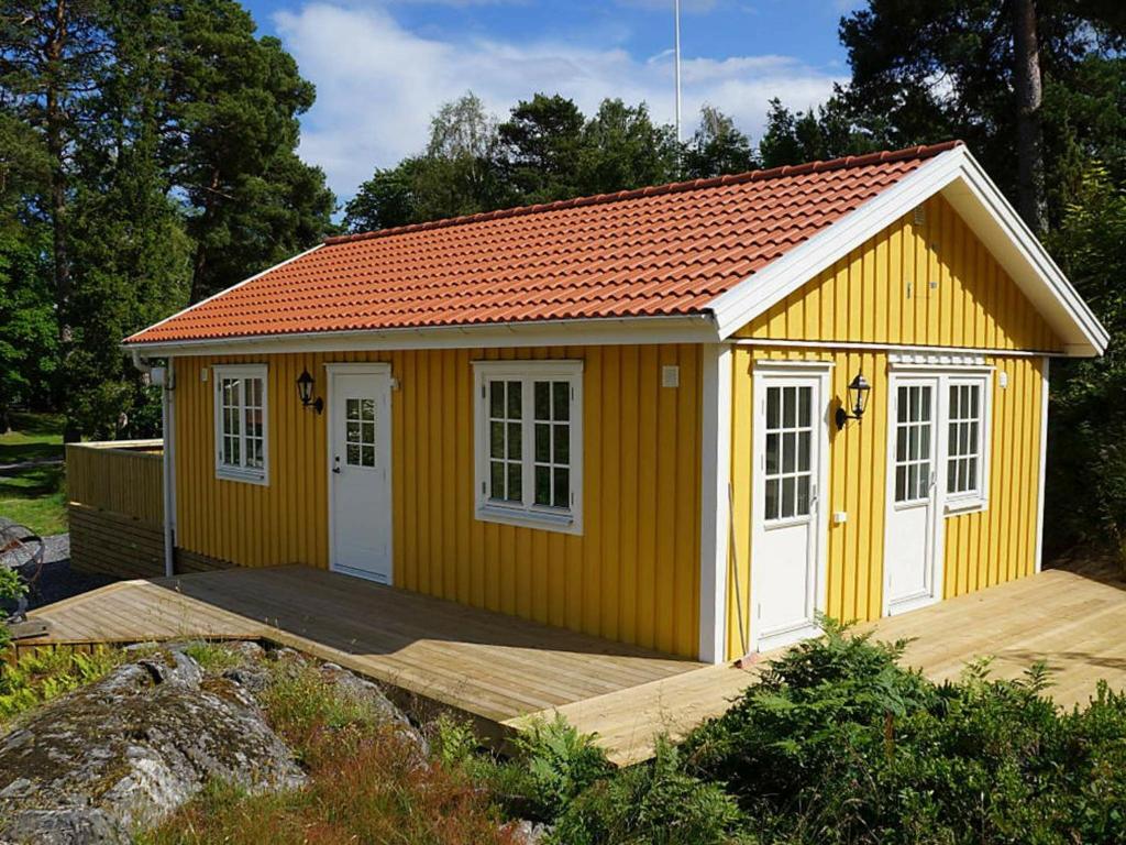 een gele schuur met witte deuren en een houten terras bij 4 person holiday home in VIKBOLANDET in Arkösund