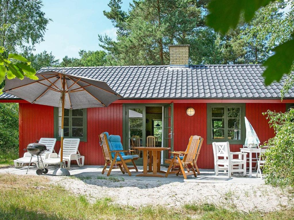 una casa roja con sillas, mesa y sombrilla en 6 person holiday home in Nex, en Snogebæk