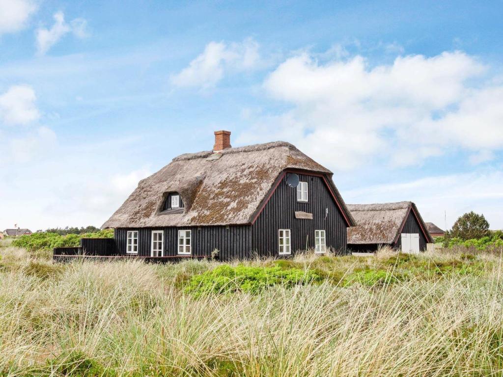 une ancienne maison noire avec un toit de chaume dans un champ dans l'établissement Holiday Home Horns Rev III, à Blåvand