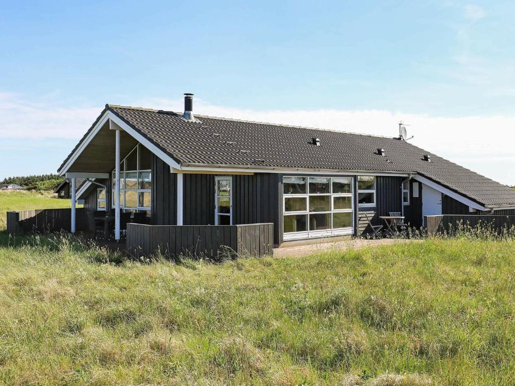 Ein schwarzes Haus auf einem Hügel mit einem Feld in der Unterkunft Holiday home Hirtshals IV in Hirtshals