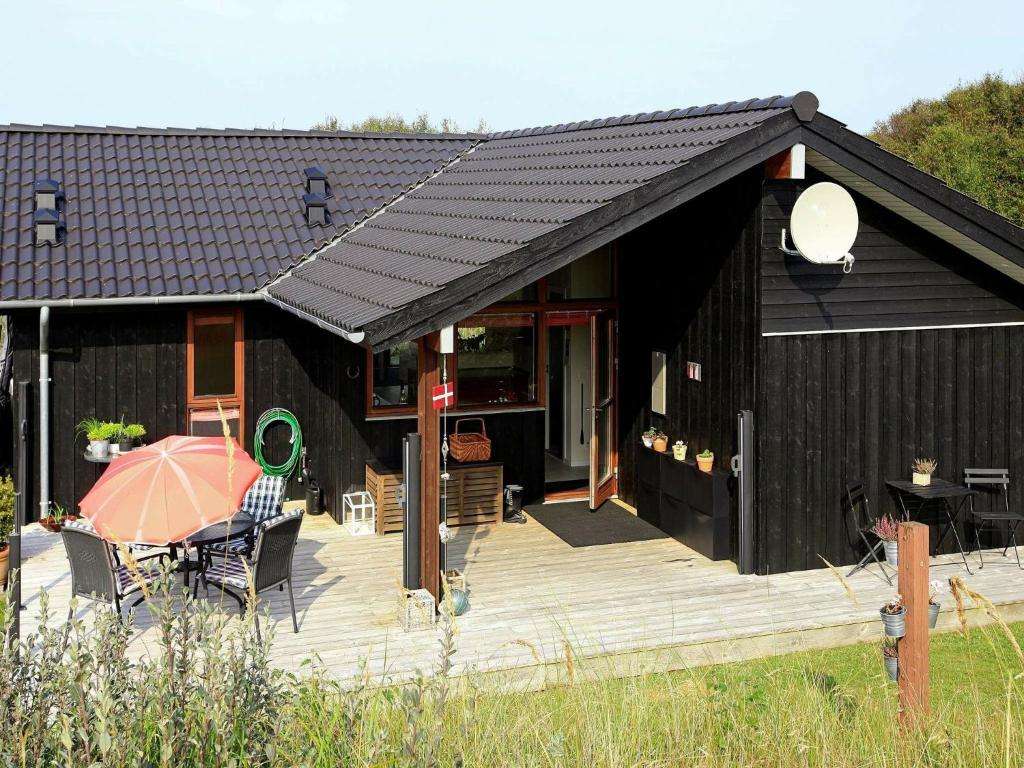 6 person holiday home in Hirtshals في هيرتسهلس: منزل أسود مع شرفة خشبية مع مظلة