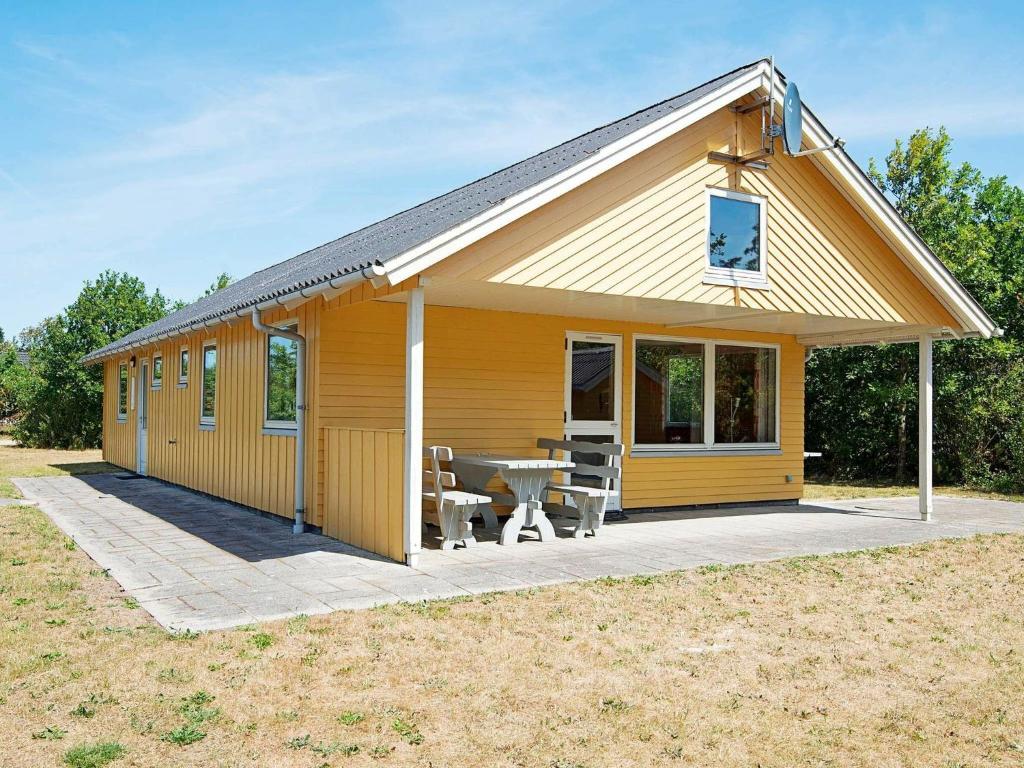 una pequeña casa amarilla con mesa y sillas en 6 person holiday home in Ulfborg en Ulfborg