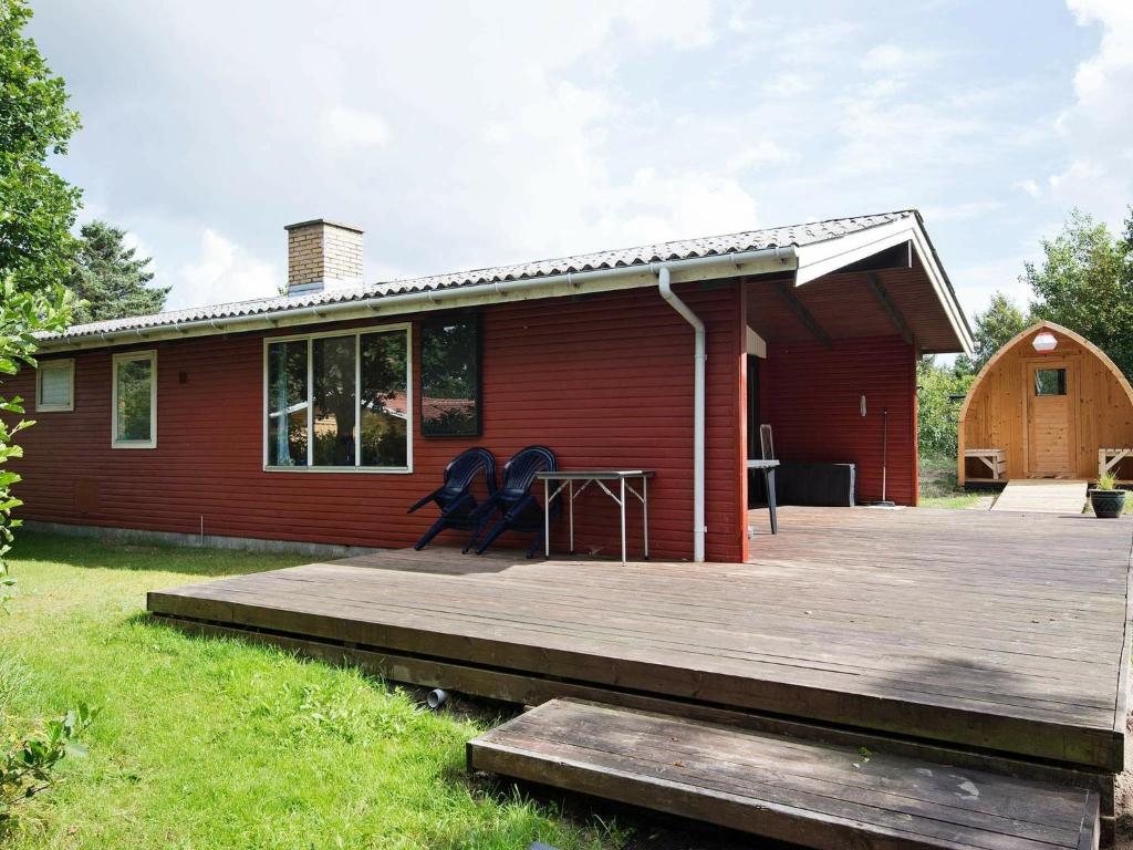 ein rotes Haus mit einer Holzterrasse davor in der Unterkunft 4 person holiday home in lb k in Ålbæk