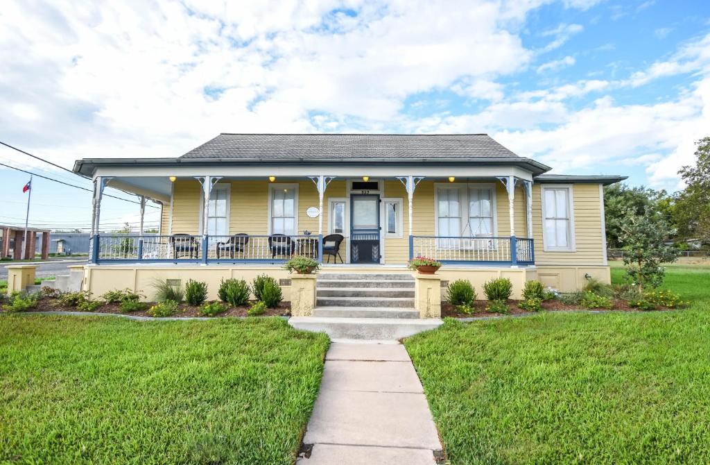 a yellow house with a porch and a lawn at Das Meyer Haus - Luxe Victorian in Schulenburg