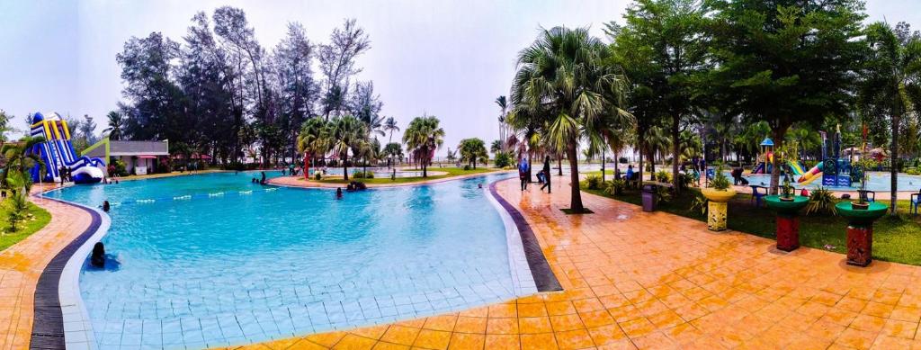a large swimming pool in a park with palm trees at De Rhu Beach Resort in Kuantan