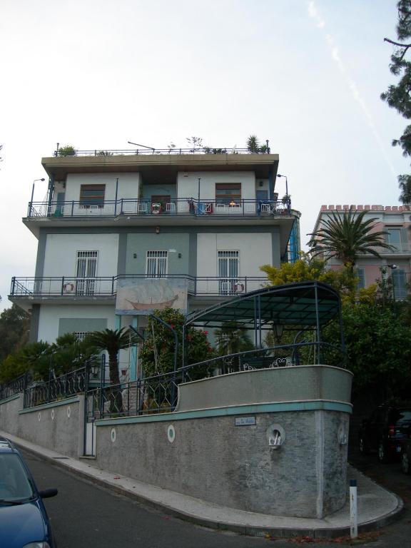 three-story building with balconies and rooftop garden on a corner street with greenery and parked cars