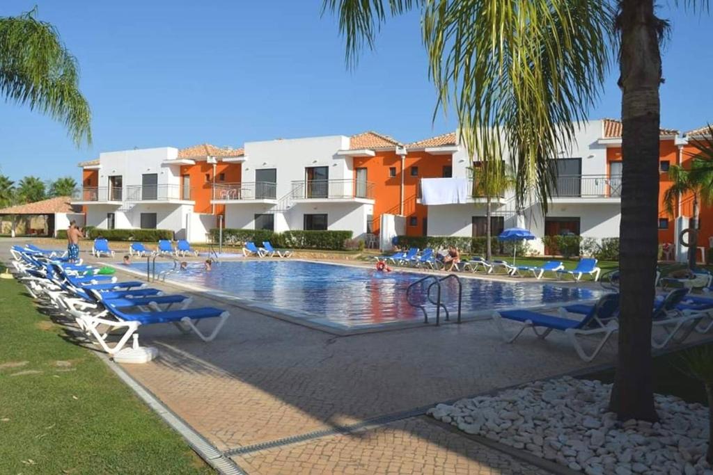 a swimming pool with chairs and palm trees and buildings at Jardins de Pera vila M in Pêra