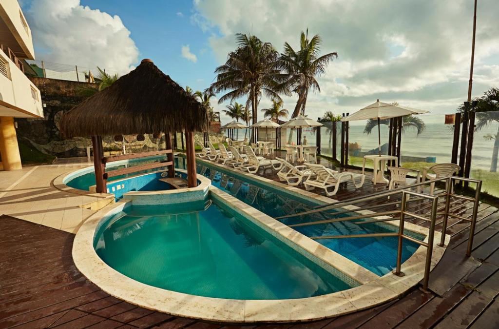 a swimming pool next to a resort with the ocean at Elegance Suítes Beira Mar in Natal