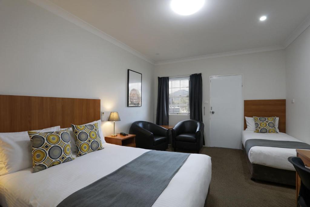 um quarto de hotel com duas camas e uma cadeira em Cadman Motor Inn and Apartments em Tamworth