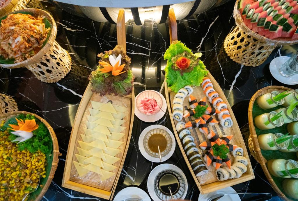 A buffet display presents sushi, sliced fruit, prepared dishes, sauces, and drinks on a dark marble table.