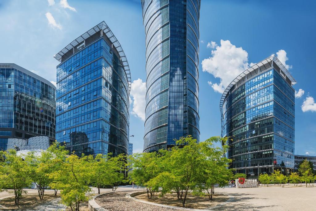 twee hoge glazen gebouwen in een stad met bomen bij P&O Apartments Plac Europejski in Warschau