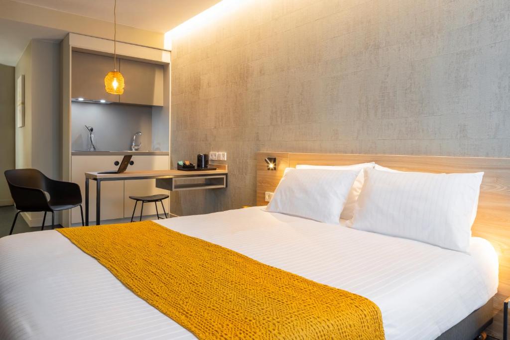 Cet appartement comprend une chambre avec un grand lit blanc et une cuisine. dans l'établissement Apparthotel 37 Lodge - Courbevoie La Défense, à Courbevoie