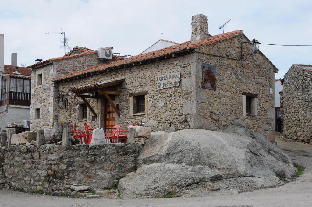 una vieja casa de piedra con una roca delante de ella en La Resbalina Casa Rural, en Cabeza del Caballo