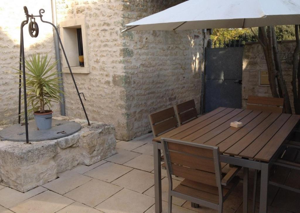 een houten tafel en stoelen onder een parasol op een patio bij L'écurie & Le Chai - Gîtes de charme entre plage et cœur de village in Dolus d'Oléron