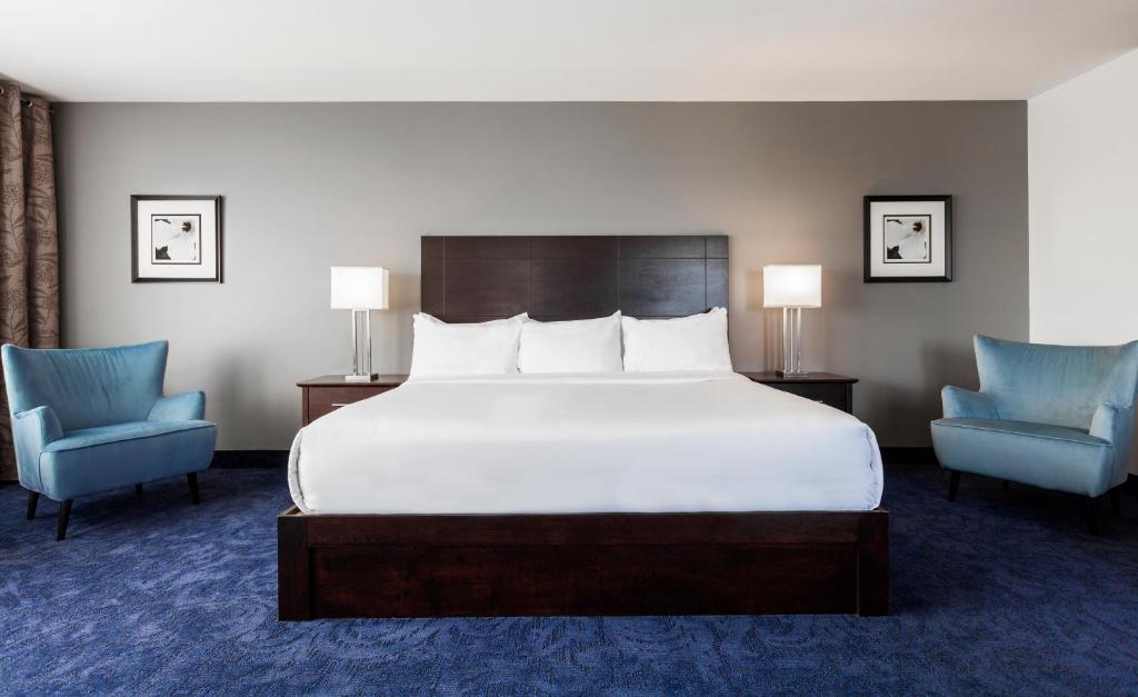 a bedroom with a large bed and two blue chairs at Imperia Hotel & Suites Saint-Eustache in Saint-Eustache