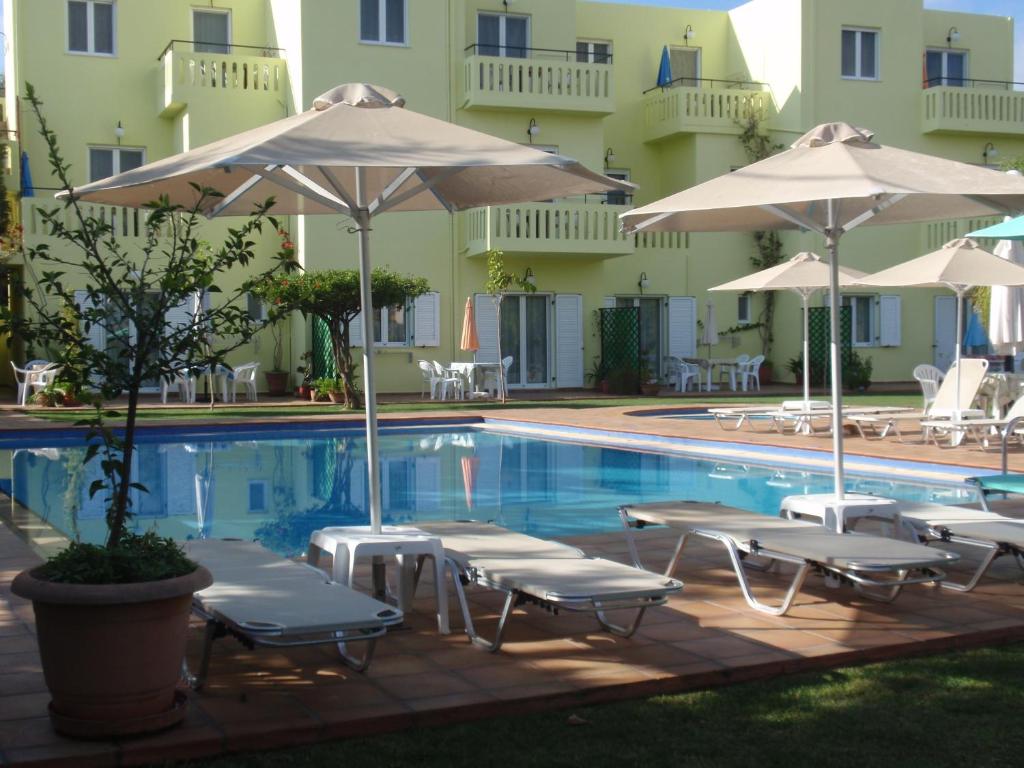 a pool with chairs and umbrellas next to a hotel at Kalithea Apartments (heated pool) in Kalyves