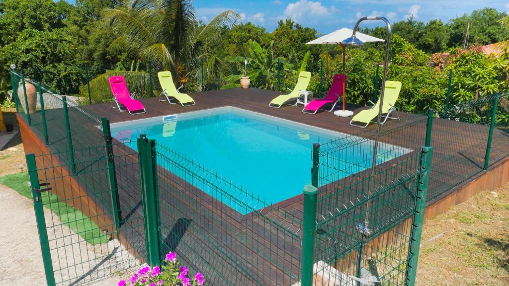a swimming pool with four chairs and an umbrella at Le Belay BAYALOCATION in Le François