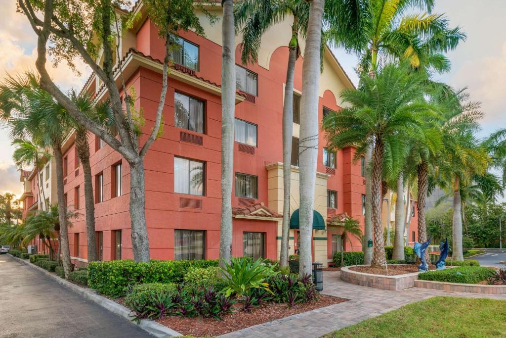 a red building with palm trees in front of it at Best Western Plus Palm Beach Gardens Hotel & Suites and Conference Ct in Palm Beach Gardens
