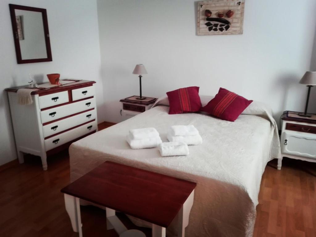 a bedroom with a white bed with red pillows and a dresser at Hostal Virgen del Rosario Cafayate in Cafayate