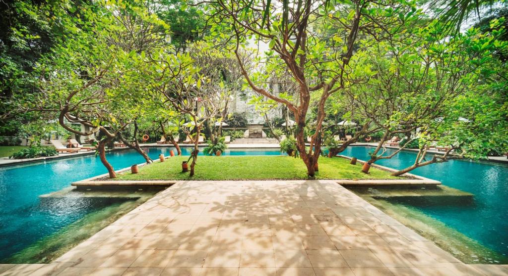 einen Fußweg in einem Park mit Bäumen und Wasser in der Unterkunft The Dharmawangsa Jakarta in Jakarta