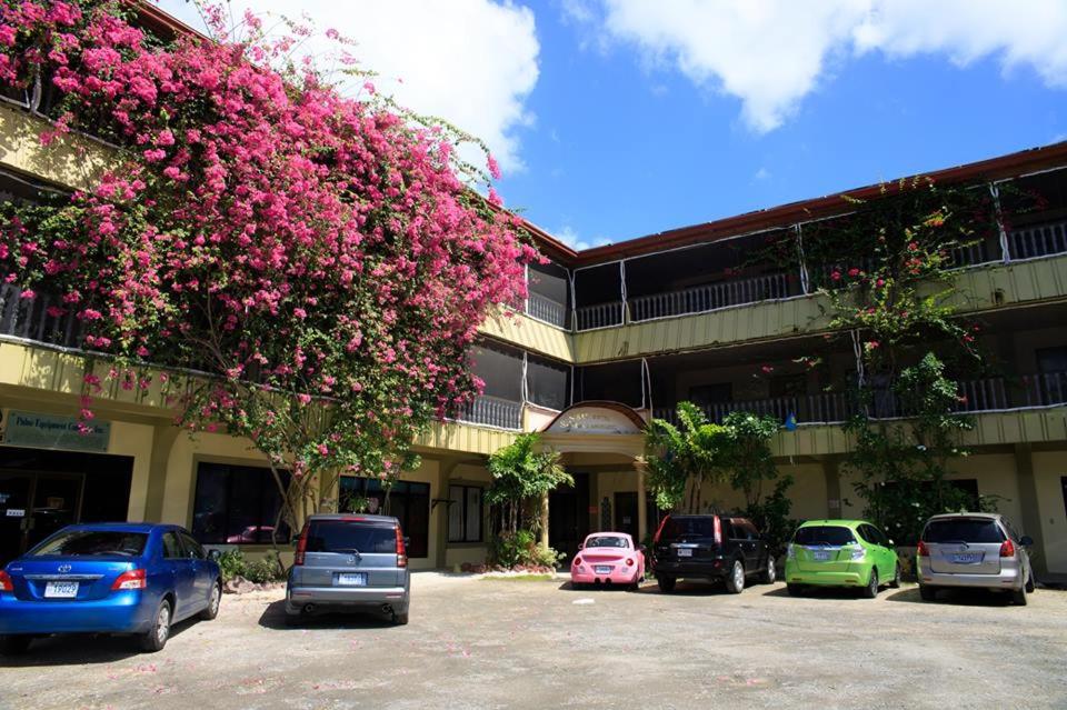 a group of cars parked in front of a building with pink flowers at S & C Hotel Suites & Apartment in Koror