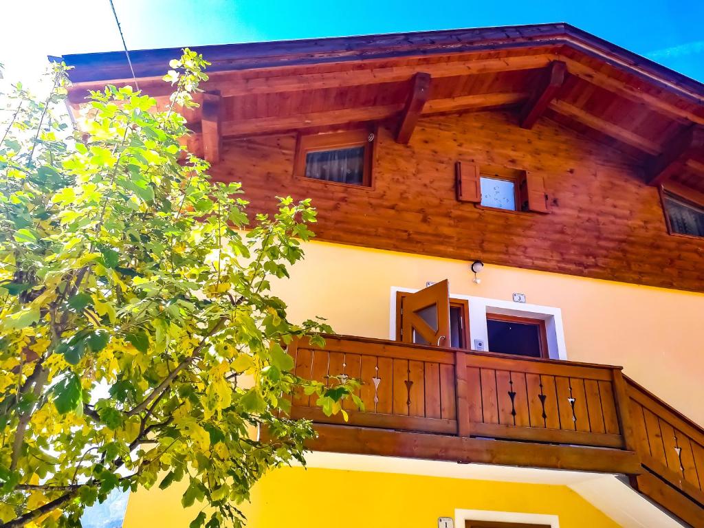 a building with a wooden balcony and a tree at Appartamento Vista Dolomiti by GoNewLocation in Moena