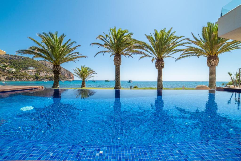 a swimming pool with palm trees and the ocean at Melbeach Hotel & Spa - Adults Only in Canyamel