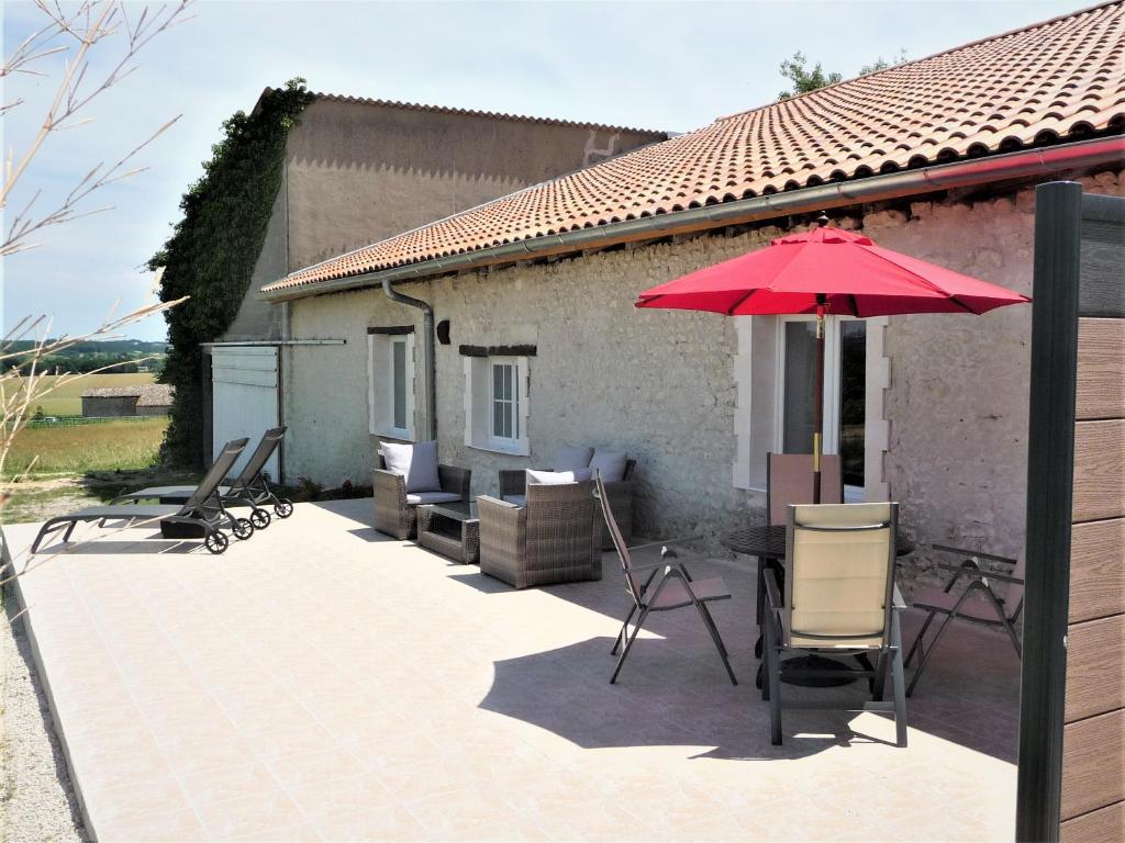 un patio con una mesa y una sombrilla roja en Le Gite Sereine, en Berneuil