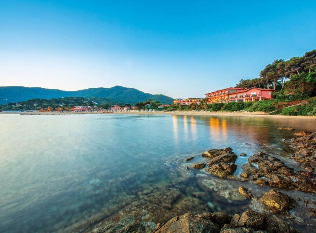 a beach with rocks in the water with houses at Hotel Del Golfo in Procchio