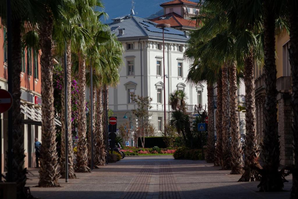 una fila di palme di fronte a un edificio bianco di Residenza Alto Garda a Riva del Garda