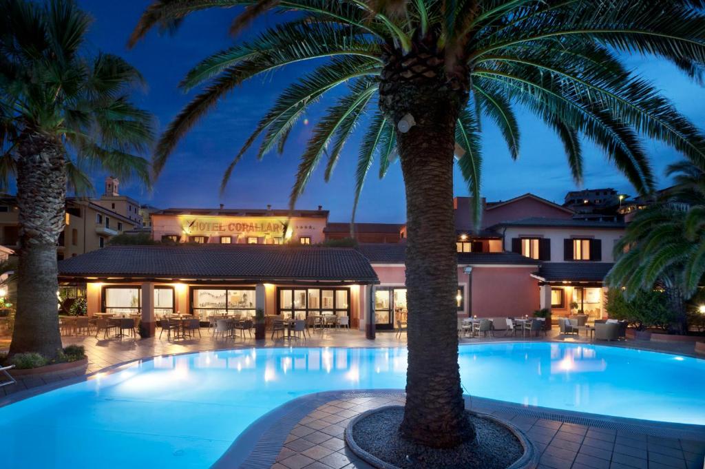 une piscine avec des palmiers en face d'un hôtel dans l'établissement Hotel Corallaro, à Santa Teresa Gallura