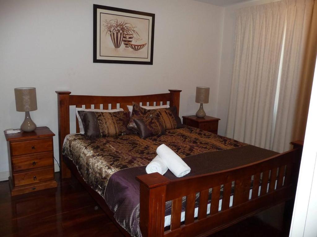 um quarto com uma cama de madeira, 2 mesas de cabeceira e 2 candeeiros. em City Getaway 3 Bedroom Adelaide's East End em Adelaide
