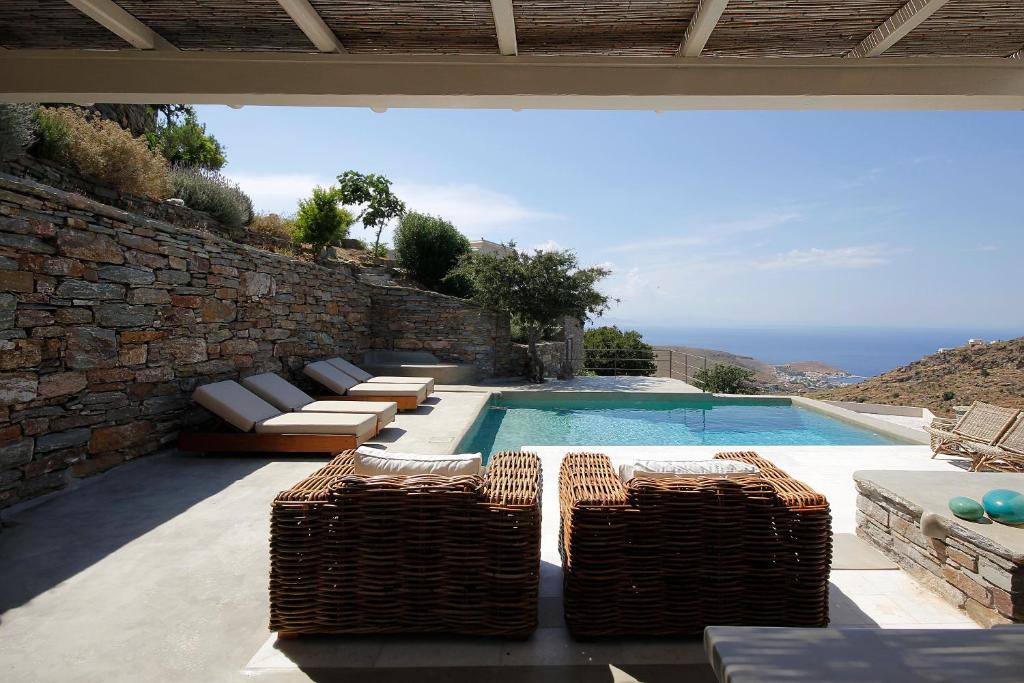 a swimming pool with wicker furniture next to a stone wall at Villa Orso Blue I in Ioulis