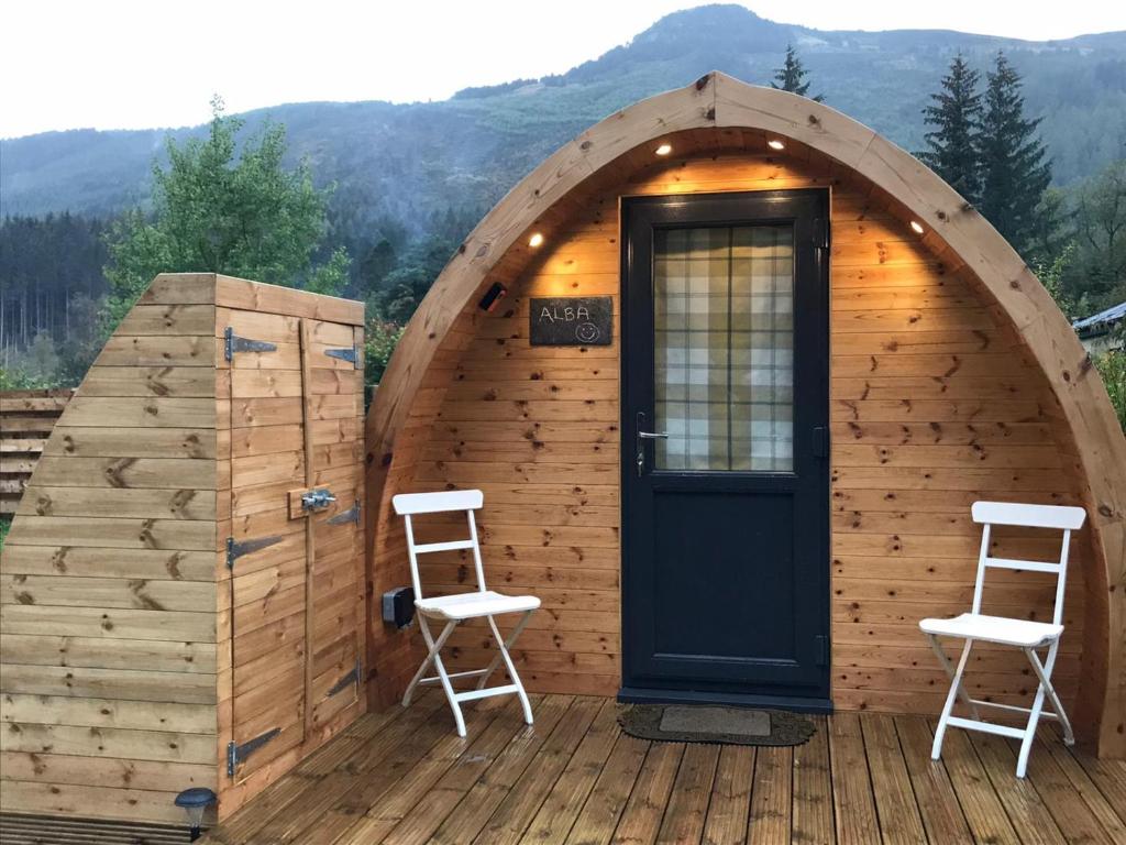 a small wooden cabin with two chairs and a door at Strathyre Camping Pods in Strathyre