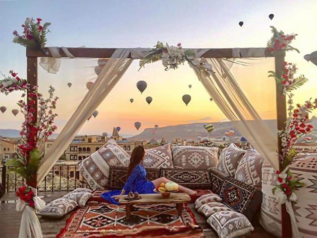 une femme assise sur un canapé qui regarde les montgolfières dans l'établissement Milat Cave Hotel, à Gorëme