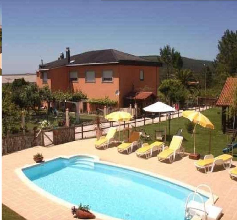 una piscina con sillas y sombrillas frente a una casa en Casa Jesús Turismo Rural en Lires