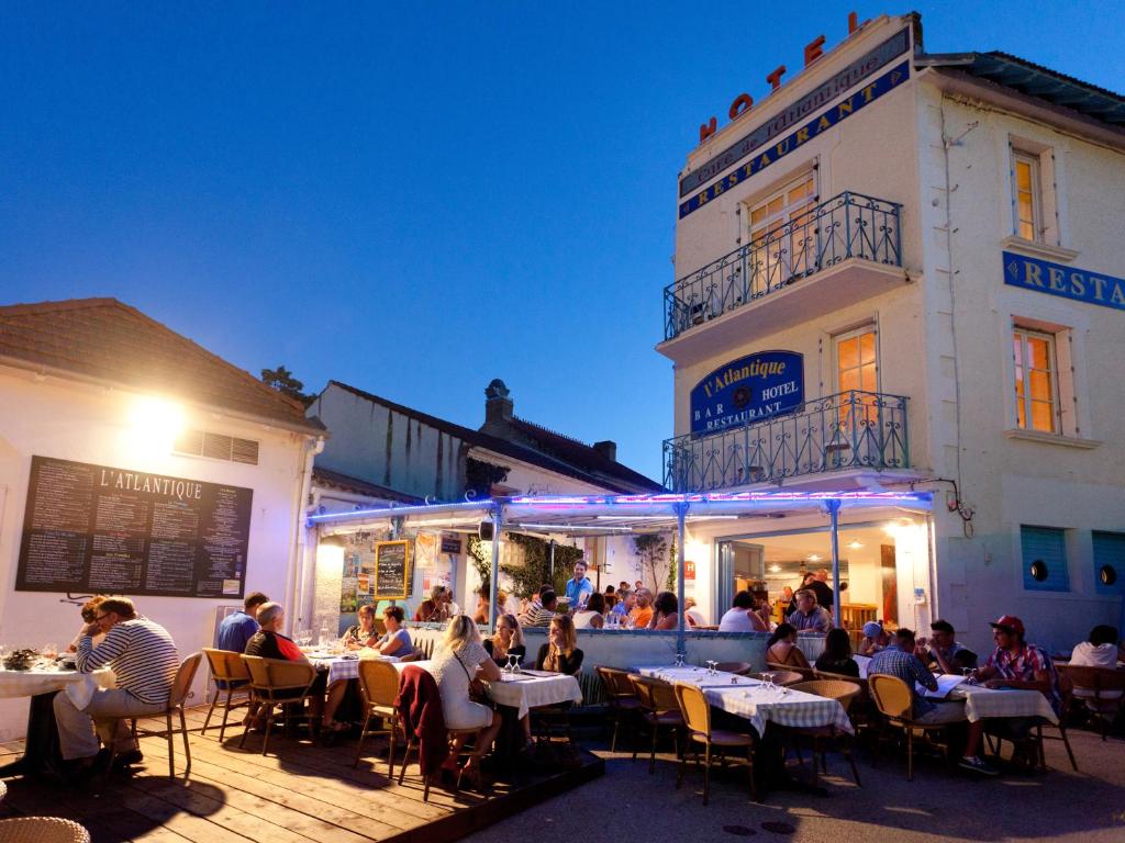 um grupo de pessoas sentadas em mesas em frente a um edifício em Hotel de l'Atlantique em La Tranche-sur-Mer