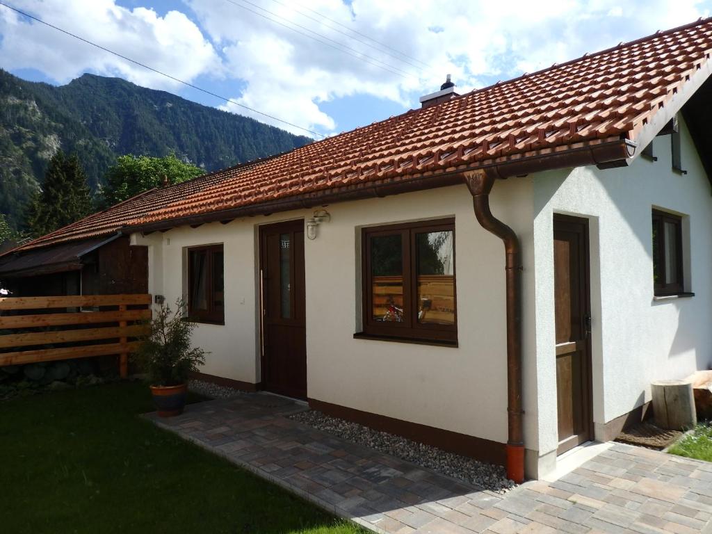 une petite maison blanche avec des montagnes en arrière-plan dans l'établissement Amsel Haus, à Bayrischzell