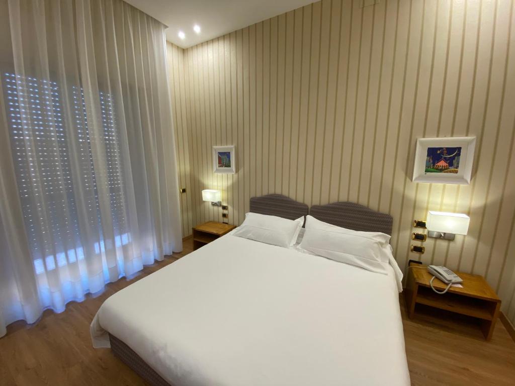 a bedroom with a large white bed and two windows at Hotel Cicolella in Foggia