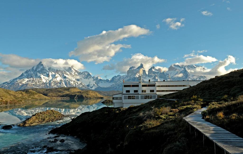 a building on a hill next to a river with mountains at Explora en Torres del Paine - All Inclusive in Torres del Paine