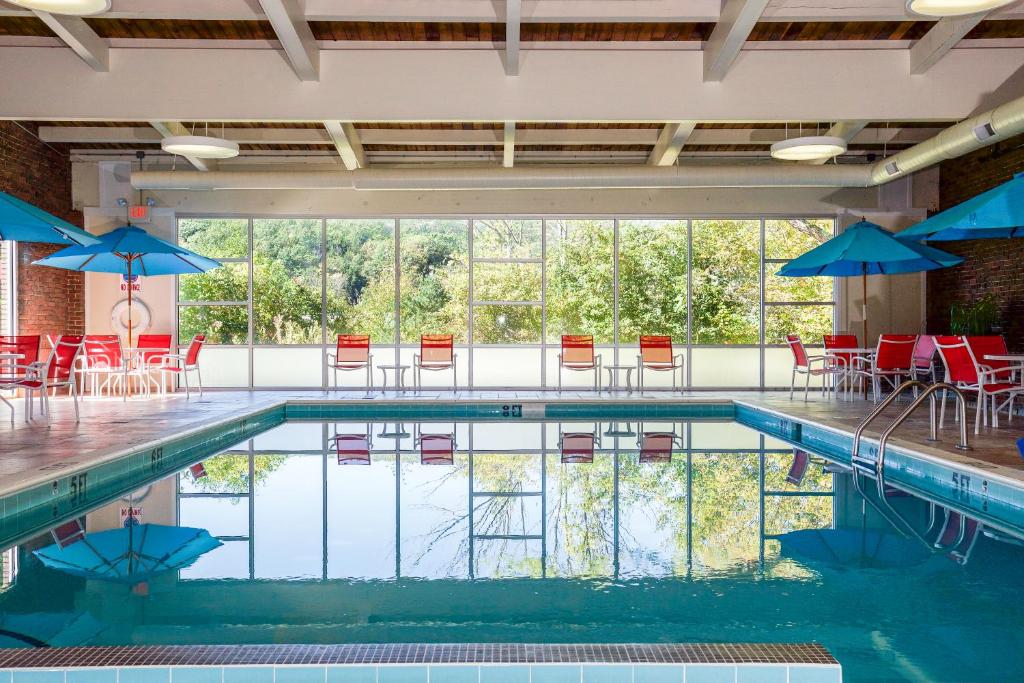 una piscina con sillas rojas y sombrillas azules en White River Inn & Suites en White River Junction