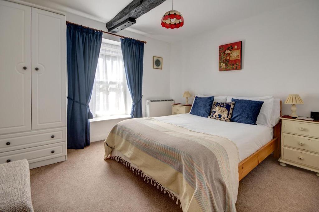 a bedroom with a bed with blue curtains and a window at Katrinas Apartment By Treetop Property in Cirencester
